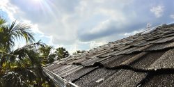 Sunlit Florida roof with curling shingles and looming storm clouds